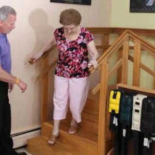 An elderly person receives assistance while descending a staircase indoors.