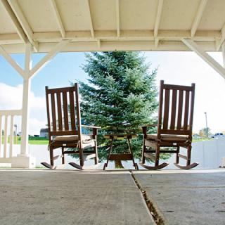 A pair of wooden rocking chairs on a covered porch facing a lush green tree.