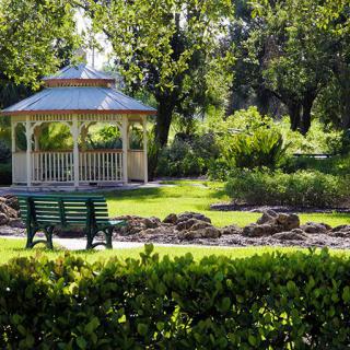 A serene park scene with a gazebo and bench surrounded by lush greenery.