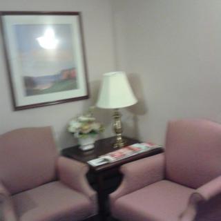 A cozy waiting room with chairs, a table, and a lamp.