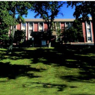 A building with a grassy lawn and trees under a clear blue sky.