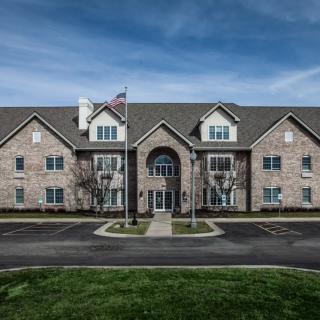 A symmetrical brick residential building with a flagpole in front and a parking lot.