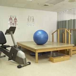 A rehabilitation room equipped with a stationary bike, an exercise ball, and a therapy platform.