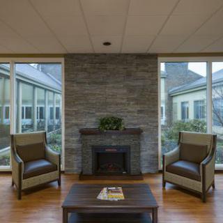 A modern living room with a stone fireplace, two chairs, and large windows.