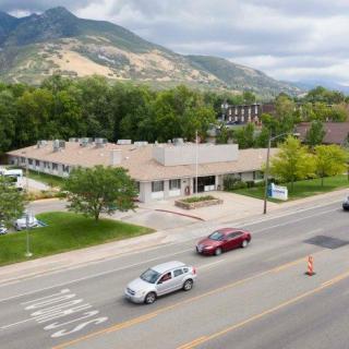 A view of a road with cars passing by, set against a backdrop of mountains and surrounded by trees on a cloudy day.