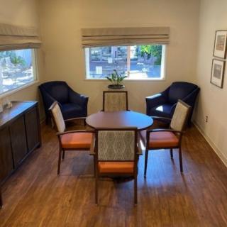 A cozy room featuring a round table surrounded by four chairs, two comfortable armchairs, and ample natural light from the windows.