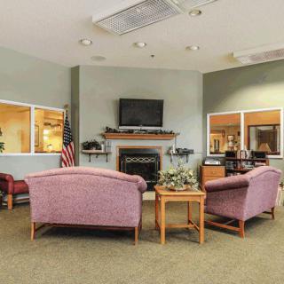 A cozy waiting room with armchairs and a fireplace, featuring a television and a coffee table.