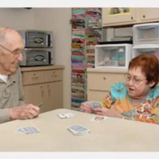 Two elderly individuals playing a card game at a table indoors.