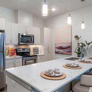 A modern kitchen with stainless steel appliances, a central island with bar stools, and pendant lighting.