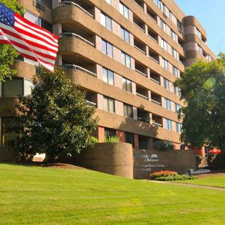 A multi-story apartment building with a well-manicured lawn and an American flag flying in front.
