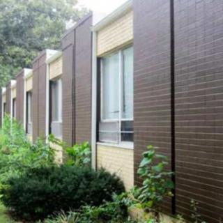A modern building exterior with rows of windows and surrounding greenery.