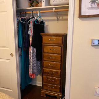 A closet with hanging clothes and a wooden chest of drawers.