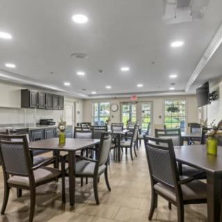 A modern dining area with multiple tables and chairs, well-lit and featuring a kitchen setup.