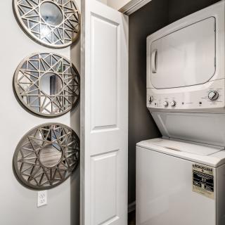 A compact laundry room with a stacked washer and dryer next to decorative mirrors.