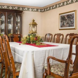A traditional dining room with a table set for guests, featuring ornate chairs and a decorative centerpiece.