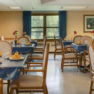 A cozy dining room set up with blue tablecloths and elegant chairs, featuring a bright window view.