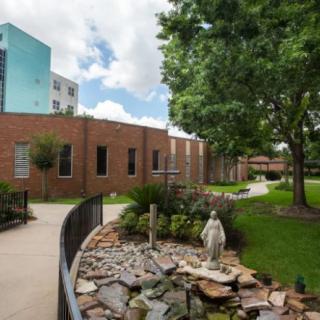 A peaceful garden with a statue and pathway beside a brick building.