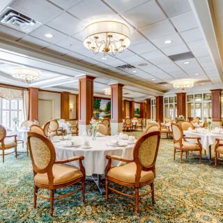 An elegant dining room with round tables, upholstered chairs, and chandeliers.