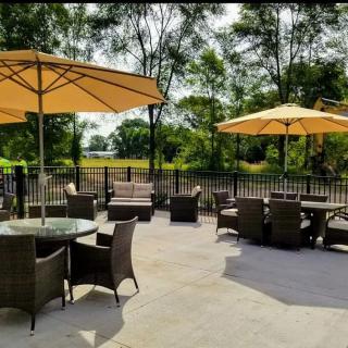 A tranquil outdoor patio with tables and chairs under large umbrellas, surrounded by trees on a sunny day.
