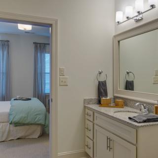 A view from the bathroom into a cozy bedroom, featuring a well-lit vanity area.