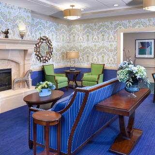 A cozy living room with elegant decor, featuring a fireplace, blue carpet, and vibrant green chairs.