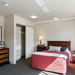 A cozy bedroom with a neatly made bed, a lamp on the nightstand, and an open closet.