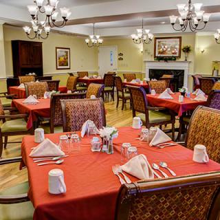 A cozy dining room setting with neatly arranged tables and chairs, decorated with red tablecloths and elegant chandeliers.