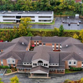 Aerial view of a healthcare facility surrounded by autumn foliage, with a parking lot and another building in the background.