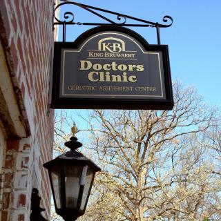 A sign for a doctor's clinic hanging outside a brick building.