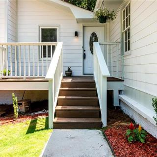A welcoming front porch with wooden steps leading to a white-sided house surrounded by landscaping.