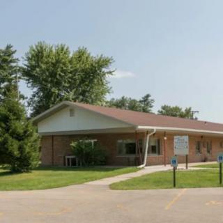 A small brick building with a sloped roof surrounded by trees and greenery.