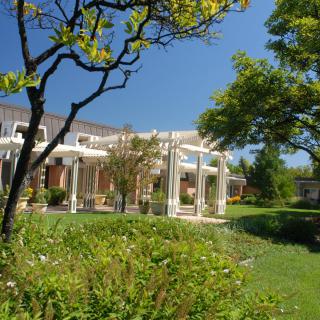 A scenic view of a building surrounded by lush gardens and trees under a clear blue sky.
