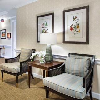 A cozy living room with two armchairs, a table with a lamp, and framed artwork on the wall.