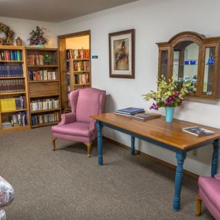 A cozy interior space with bookshelves, armchairs, and a decorative table with flowers.