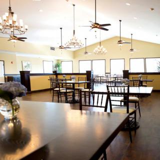 A spacious restaurant interior with wooden tables and chairs, illuminated by elegant chandeliers and ceiling fans.