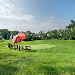 A peaceful golf course with a bench and red umbrella near the green.