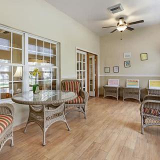 A cozy living room with wicker furniture, large windows, and a ceiling fan.