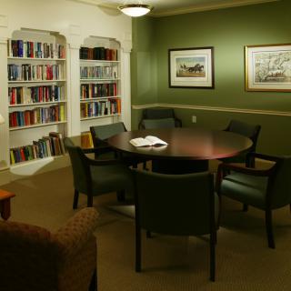 A cozy meeting room with bookshelves and a round table surrounded by chairs.