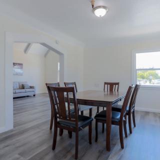 A minimalist dining room with a wooden table and chairs, featuring bright natural lighting.