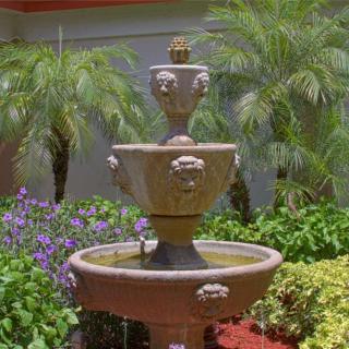 A decorative tiered fountain surrounded by lush greenery and vibrant flowers in a serene garden setting.