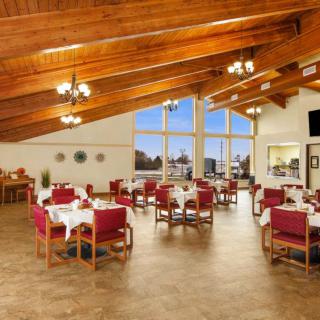 A spacious dining area with wooden ceiling, elegant chandeliers, and large glass windows at sunset.