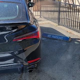 A black car parked beside a fence, showing the rear and part of the license plate area.