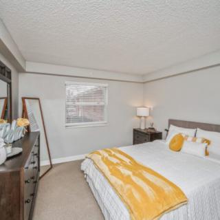 A modern bedroom with neutral tones and yellow accents, featuring a large bed, a mirror, and stylish decor.