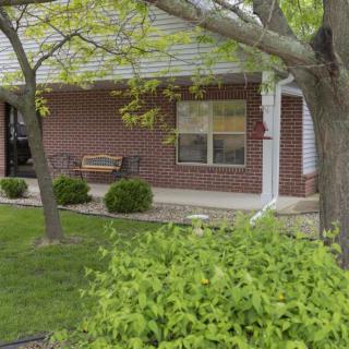 A suburban house with a brick exterior, featuring a porch swing and surrounded by trees and bushes.