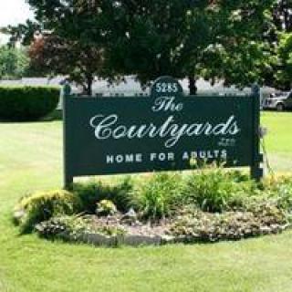 Sign indicating 'The Courtyards' home for adults, surrounded by landscaping and greenery.