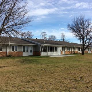 A suburban single-story house with a lawn and trees under a blue sky.