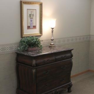 A classic chest of drawers with a lamp and framed artwork in a cozy hallway.