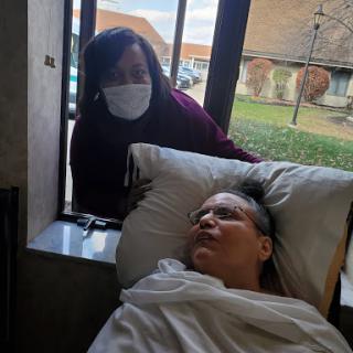 A caregiver tends to a patient in a hospital room, providing comfort and support.
