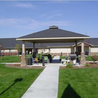 A gazebo with a paved pathway surrounded by a well-maintained lawn under a clear sky.
