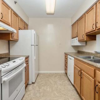 A narrow kitchen featuring wooden cabinets, white appliances, and a tile floor.
